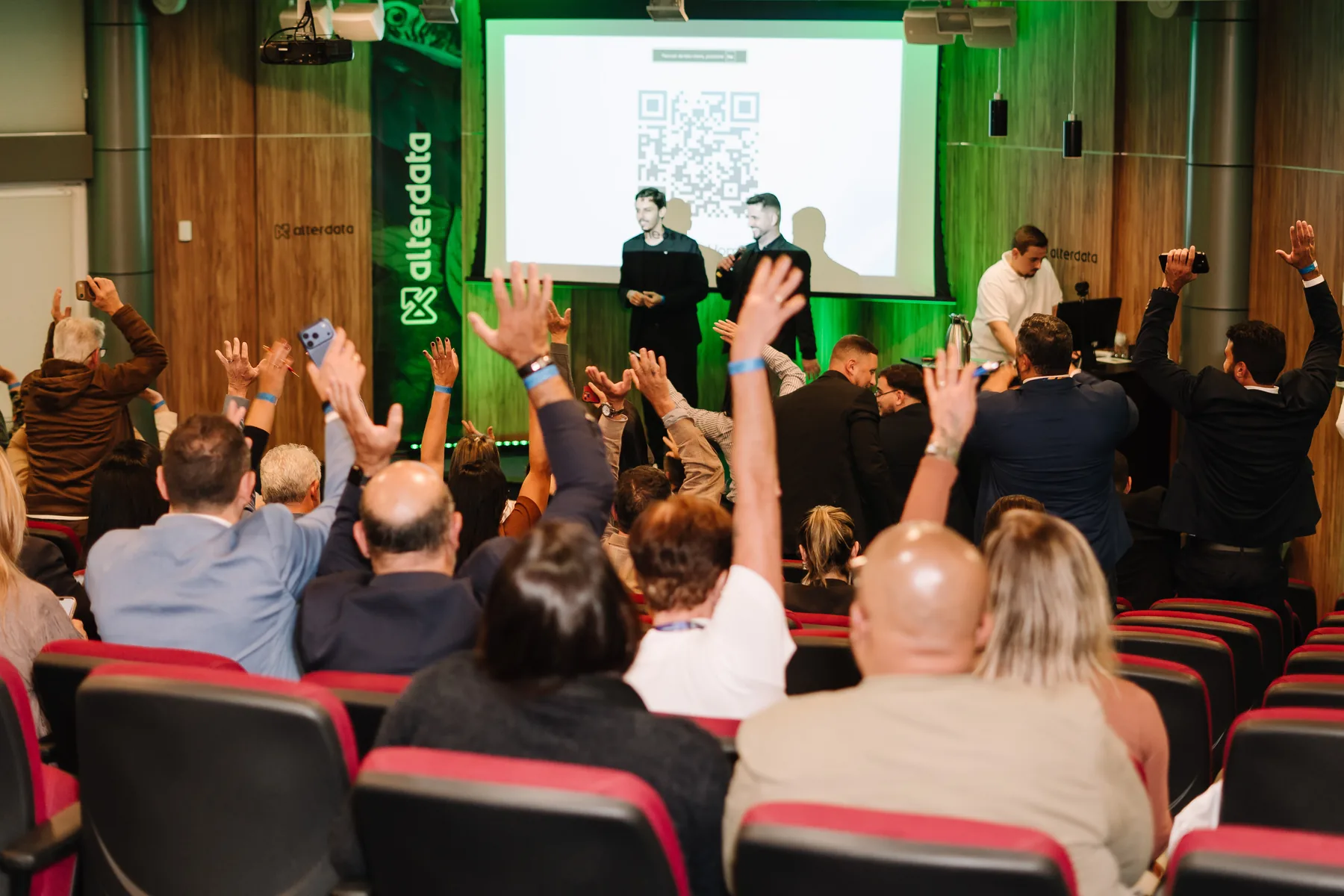 Plateia da 1ª edição do IMOB Experience com as mãos levantadas respondendo a uma pergunta do palco